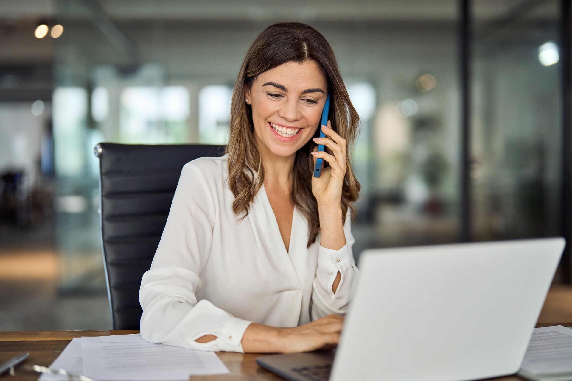 Happy mature business woman talking on phone making business call in office.